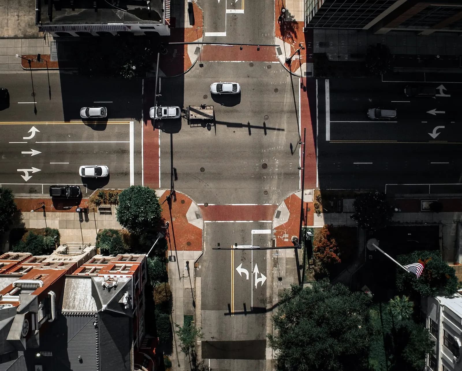 Aerial view straight down on a downtown intersection with brick crosswalks, turn-lane arrows and parked cars.